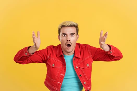 Surprised gay man gesturing and looking at the camera in studio with yellow background