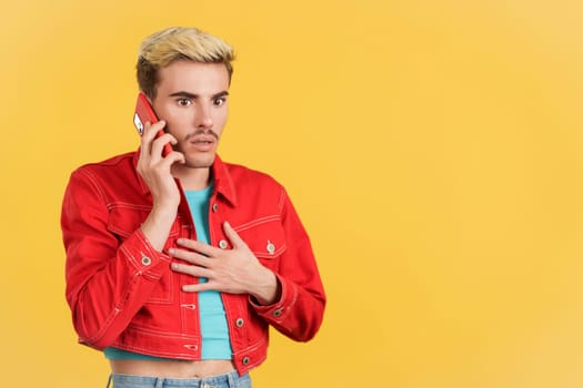 Astonished gay man talking to the mobile in studio with yellow background