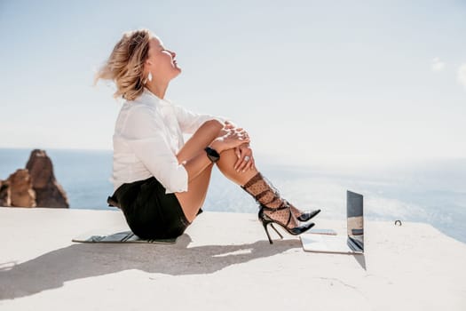 Happy girl doing yoga with laptop working at the beach. beautiful and calm business woman sitting with a laptop in a summer cafe in the lotus position meditating and relaxing. freelance girl remote work beach paradise