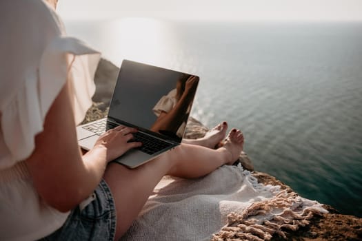 Woman sea laptop. Business woman in yellow hat working on laptop by sea. Close up on hands of pretty lady typing on computer outdoors summer day. Freelance, digital nomad, travel and holidays concept.