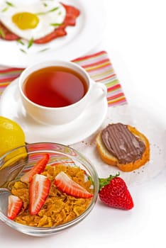 Bowl of tasty crispy corn flakes with milk and strawberries on white