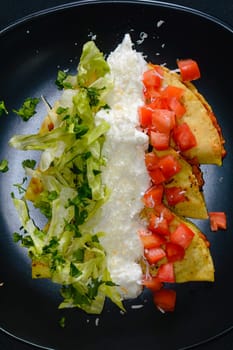 Mashed potato and chorizo fried tacos dorados with lettuce, tomatoes, sour cream and cotija cheese. Shot on black background.