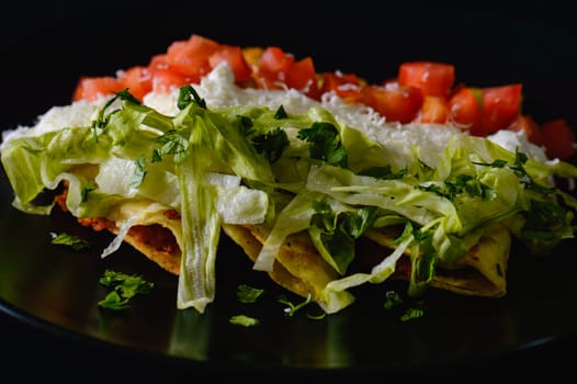 Mashed potato and chorizo fried tacos dorados with lettuce, tomatoes, sour cream and cotija cheese. Shot on black background.