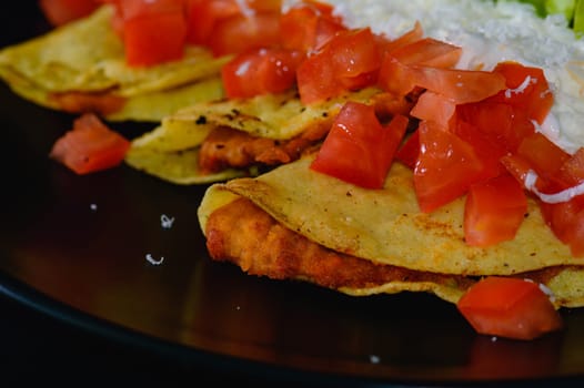 Mashed potato and chorizo fried tacos dorados with lettuce, tomatoes, sour cream and cotija cheese. Shot on black background.