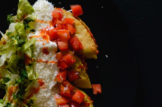 Mashed potato and chorizo fried tacos dorados with lettuce, tomatoes, sour cream and cotija cheese. Shot on black background.