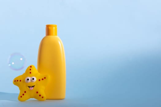 Yellow plastic bottle with baby cosmetic and funny bath toy. Soap bubbles on a background. The concept of children's bath time