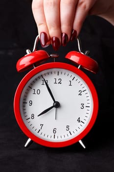 Female arm hold up red alarm clock dial on black background with five before eight oclock early morning closeup