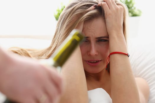 beautiful young blond woman stay in bad is given bottle of wine unhealthy way of life concept