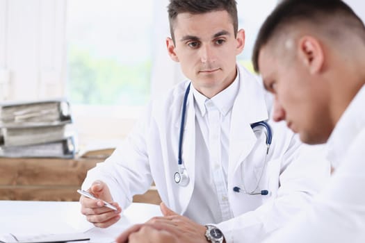 Handsome male medicine doctor with clipboard pad in hands examine patient and prescribe remedy. Exam visitor reception disease prevention ward round visit check 911 healthy lifestyle concept