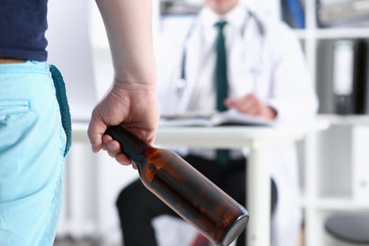 Alcoholic hold in hand empty bottle at doctor reception office closeup. Grief and despair, intoxicated, change life, drunkenness lifestyle sobriety and temperance bad habit dependence concept