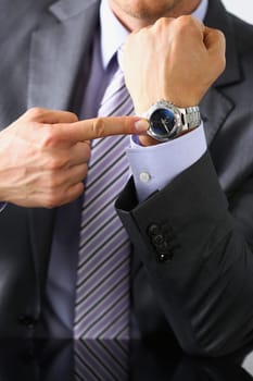 Man in suit and tie check out time at silver wristwatch closeup. Show and point with finger waste minute modern punctual life style start hurry job idea last second clockwork precision concept