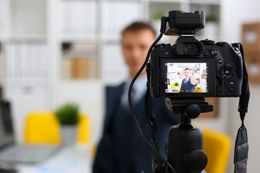 Male in suit and tie show confirm sign arm making promo videoblog or photo session in office camcorder to tripod closeup. Vlogger promotion selfie solution or finance advisor management information