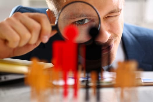 Man in suit look thru loupe on statuettes closeup in office. Success hr assessment people headhunt inspector applicant exchange concept
