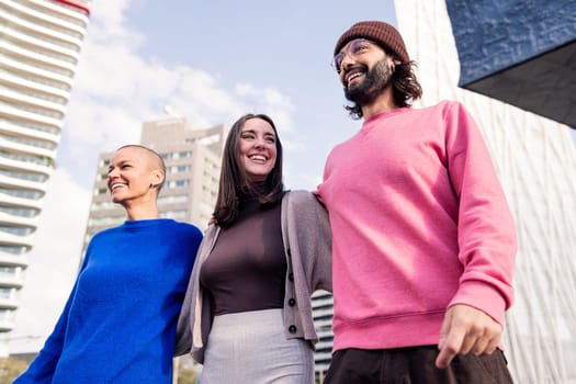 three joyful friends, one man and two women, laughing and hugging during a stroll together on a sunny day, concept of friendship and urban lifestyle