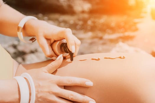 Sexy Woman in bikini apply sun protection cream on her smooth tanned legs. Skin care. Legs on the beach. Portrait of female in hat smearing moisturizing lotion. Sunblock concept.