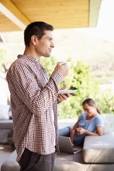 Enjoying the beauty of nature with a few modern comforts. a young man drinking coffee while a woman works on a laptop in the background