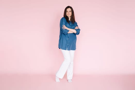 Confident businesswoman in smart casual attire standing with folded hands in front of pink background - Full body shot for professional profile or website banner