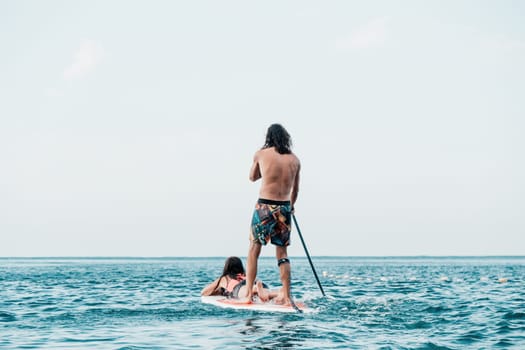 Silhouette of woman standing, surfing on SUP board, confident paddling through water surface. Idyllic sunset or sunrise. Sports active lifestyle at sea or river.