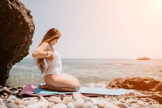 Young woman with black hair, fitness instructor in pink sports leggings and tops, doing pilates on yoga mat with magic pilates ring by the sea on the beach. Female fitness daily yoga concept