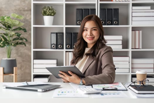 Young successful businesswoman at workplace is satisfied with results of achievement at work smiling and using tablet computer.