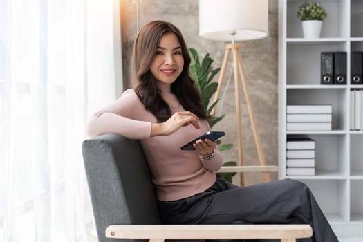 Smiling woman rest sit on sofa in living room texting messaging on smartphone, happy mature female browse wireless internet or shopping online, using cellphone gadget at home.