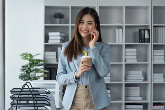 Confident business woman attractive smiling holding coffee talking on the phone and looking at camera in smart in office.