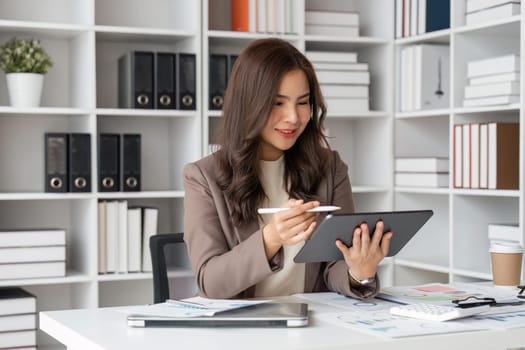 Young successful businesswoman at workplace is satisfied with results of achievement at work smiling and using tablet computer.