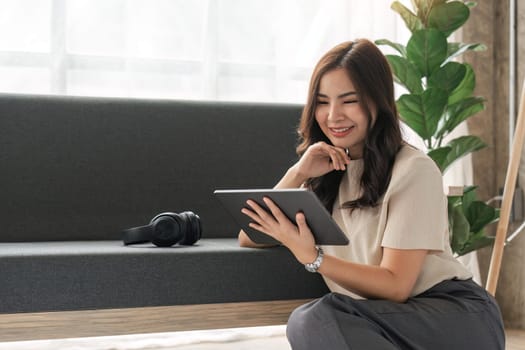 Smiling woman rest sit on sofa in living room texting messaging on digital tablet happy mature female browse wireless internet or shopping online, using digital tablet gadget at home.
