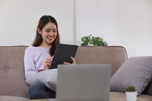 Smiling woman rest sit on sofa in living room texting messaging on digital tablet happy mature female browse wireless internet or shopping online, using digital tablet gadget at home.