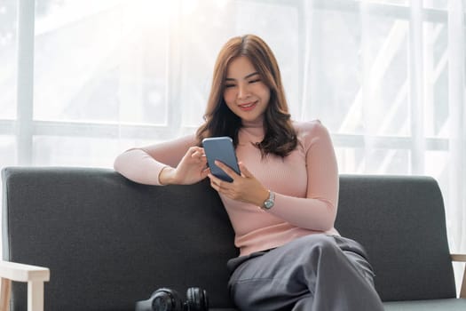 Smiling woman rest sit on sofa in living room texting messaging on smartphone, happy mature female browse wireless internet or shopping online, using cellphone gadget at home.