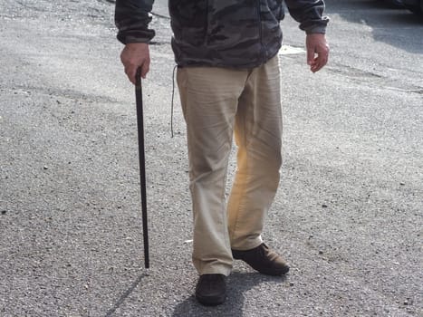 Macro shot of elderly unrecognizable man holding the wooden handle of a wppd walking cane, outdoors in the street