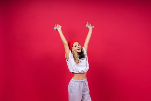 Kid girl doing fitness exercises with dumbbells on a red background