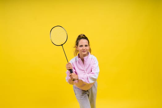 Full length studio photo of ten year old girl holding a badminton racket and isolated on yellow.