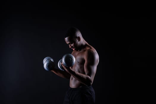 Isolated african muscular man with dumbbells on a dark studio background. Strong shirtless black guy