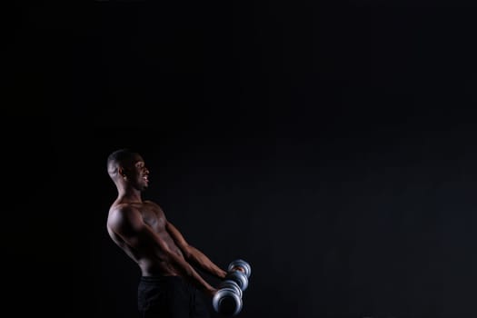 Isolated african muscular man with dumbbells on a dark studio background. Strong shirtless black guy