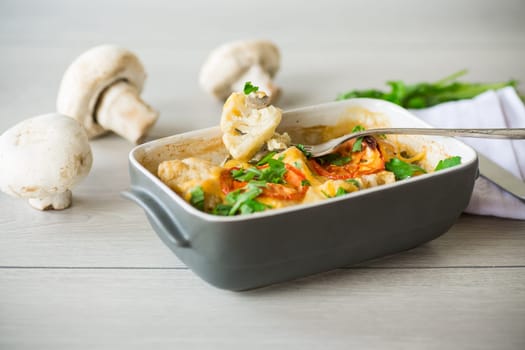 cauliflower baked with chicken fillet and mushrooms under cheese in a ceramic form, on a wooden table.