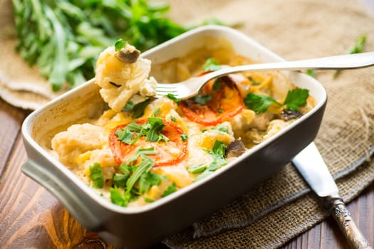 cauliflower baked with chicken fillet and mushrooms under cheese in a ceramic form, on a wooden table.