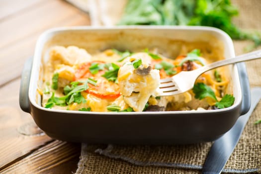 cauliflower baked with chicken fillet and mushrooms under cheese in a ceramic form, on a wooden table.