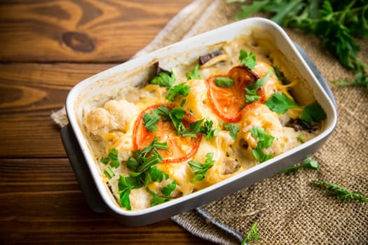 cauliflower baked with chicken fillet and mushrooms under cheese in a ceramic form, on a wooden table.