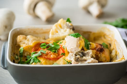 cauliflower baked with chicken fillet and mushrooms under cheese in a ceramic form, on a wooden table.