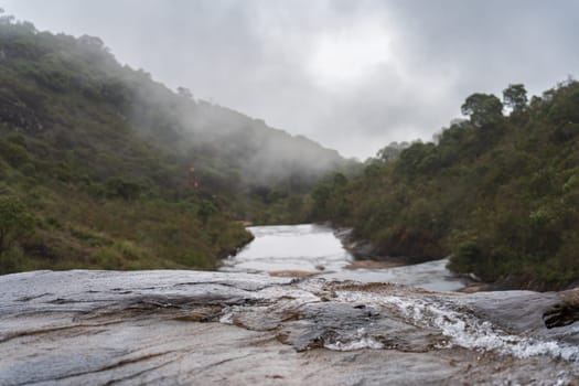 A mystical misty waterfall edge with a green jungle backdrop and flowing water down below.