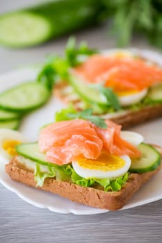 fried toast with lettuce, egg, cucumbers and red fish in a plate, on a wooden table.