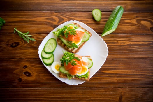 fried toast with lettuce, egg, cucumbers and red fish in a plate, on a wooden table.
