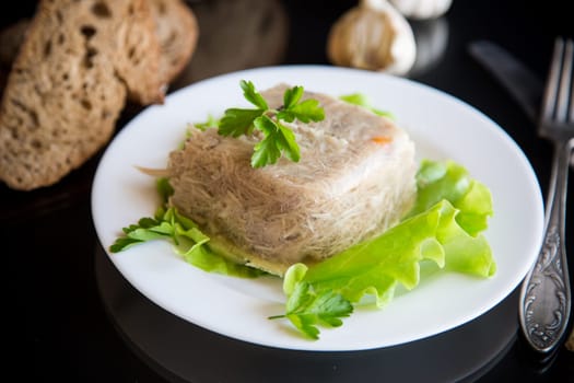 Boiled chicken meat aspic in meat gelatin broth in a plate on a black background