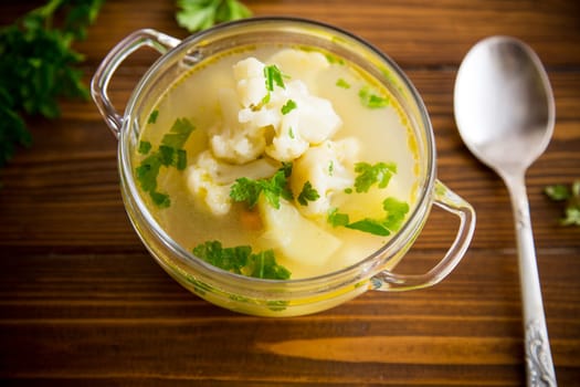 cooked chicken soup with cauliflower and vegetables in a bowl on a wooden table