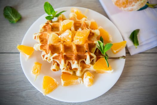 Cooked sweet Belgian waffles with oranges on a wooden table.