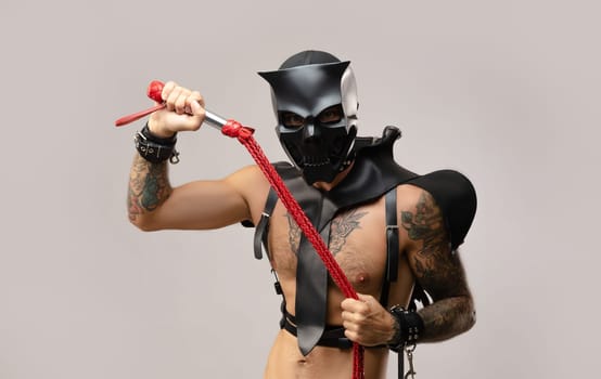 sexy a man in a bdsm skull mask, dressed in a leather raincoat with leather handcuffs and straps on the body on a light background of copy paste
