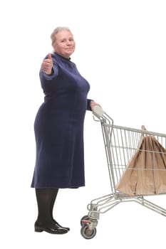 Cheerful mature lady with a shopping cart giving a thumb up isolated on white background