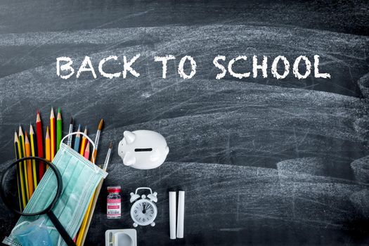 Back to school or college concept. Top view of school supplies stationery and surgical face mask on blackboard background, Back to safe education new normal during outbreak coronavirus pandemic