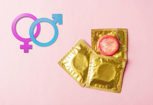 World sexual health or Aids day, Top view flat lay condom in wrapper pack tear open and Male, female gender signs, studio shot isolated on pink background, Safe sex and reproductive health concept